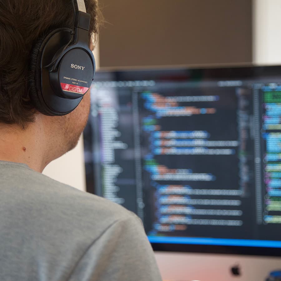 A man wearing headphones looks at code on a computer screen.